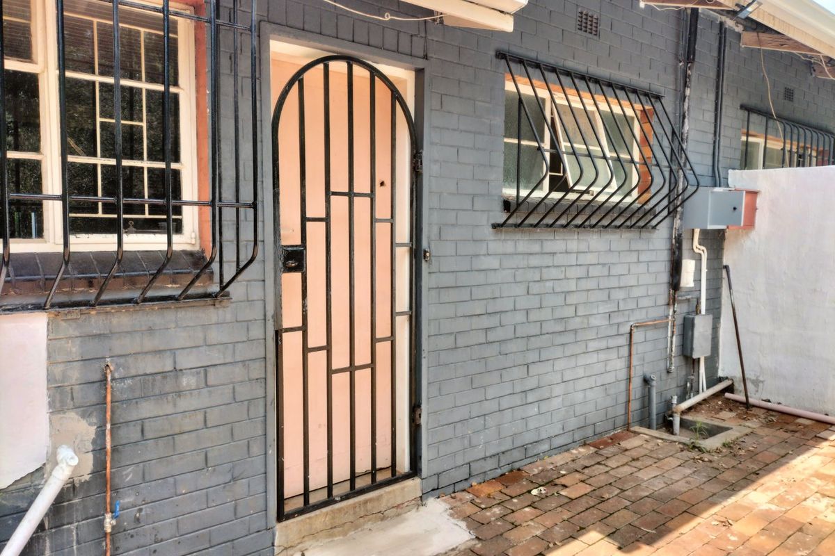 Rear exterior view of an apartment featuring painted brick walls, security gates, window bars, and brick paved ground area.