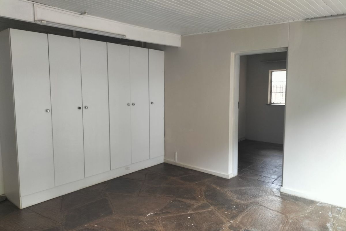An empty bedroom featuring built-in cupboards, stone tile flooring, and a tongue and groove ceiling, leading into an adjacent room.