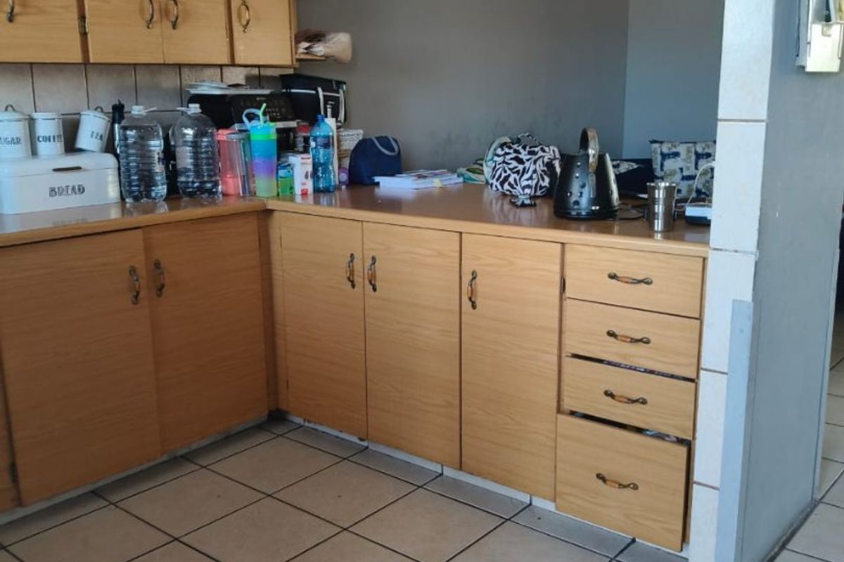A dated kitchen featuring laminate cabinetry, ceramic floor tiles, and a tiled splashback, offering potential for a modern renovation.