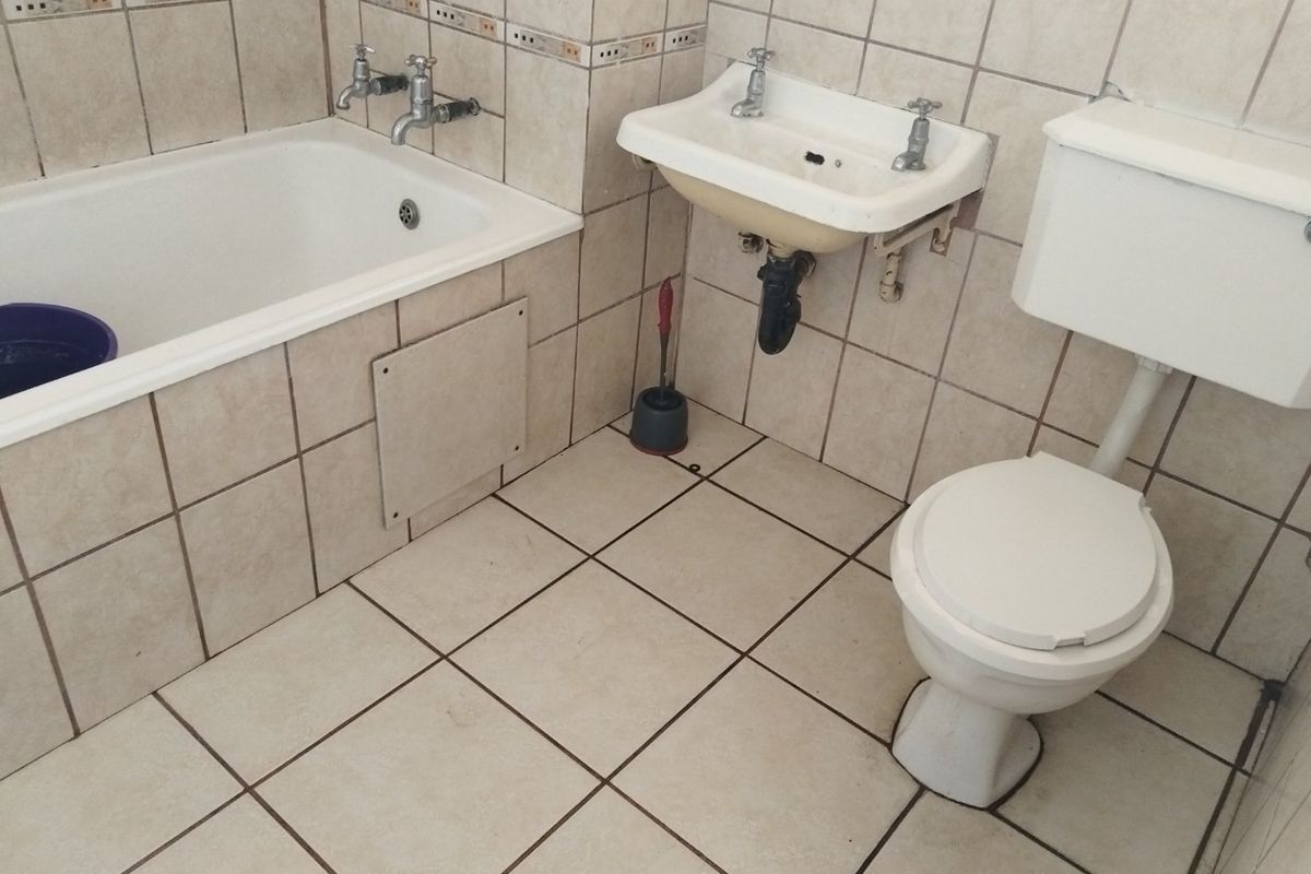 A dated bathroom featuring a standard bathtub, wall-mounted basin, and toilet with neutral ceramic tiling throughout.