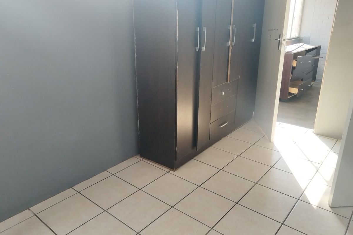 A bedroom featuring ceramic floor tiles and a built-in dark wood wardrobe with visible signs of wear.