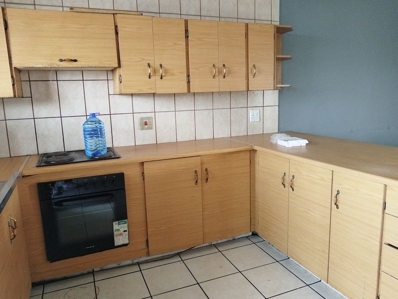A dated kitchen featuring laminate cabinetry, built-in oven, electric hob, and tiled backsplash, requiring cosmetic updates to modernize the space.
