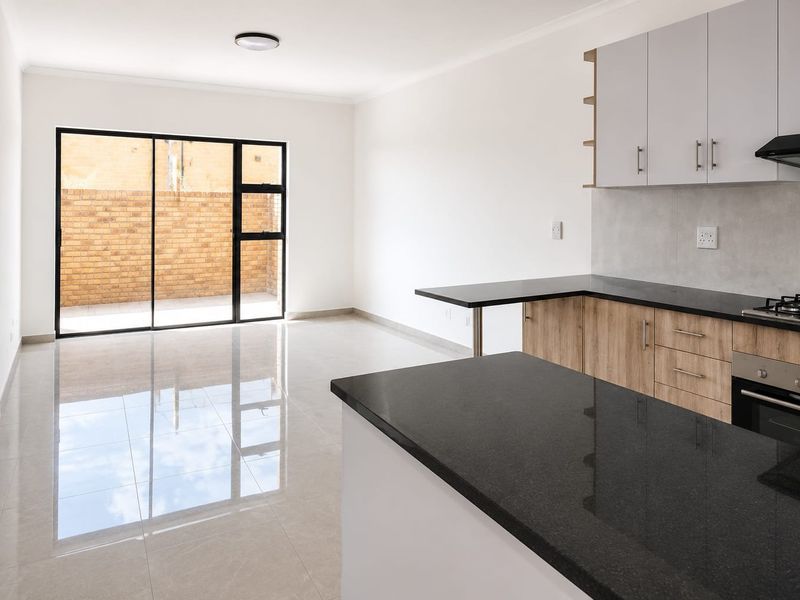 Modern open-plan kitchen and living area featuring sleek granite countertops, built-in appliances, tiled flooring, and direct access to an outdoor patio area.