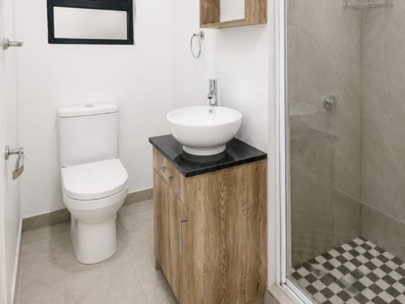 Modern bathroom featuring a vessel sink vanity, glass-enclosed shower with patterned floor tiles, and neutral wall tiling.