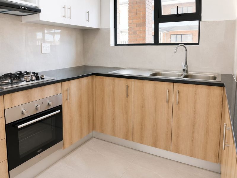 Modern kitchen featuring light wood cabinetry, granite countertops, a gas hob, built-in oven, and a stainless steel sink with tiled finishes.