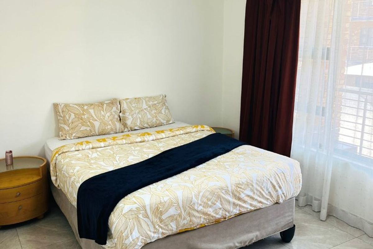 A well-lit bedroom featuring neutral tiled flooring and large windows with curtain rails, providing a clean and functional living space.