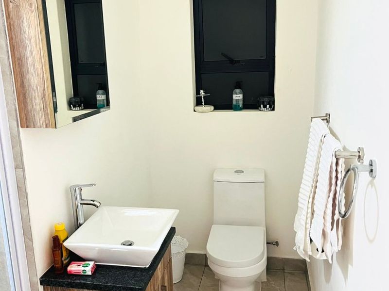 A modern bathroom featuring a vessel sink on a wood-finish vanity, a toilet, and tiled flooring with a window for natural light.
