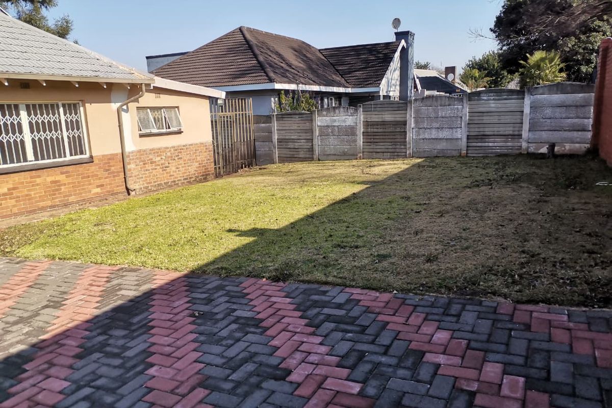 A rear exterior view featuring a paved driveway, a lawn area, and a secure precast concrete boundary wall.