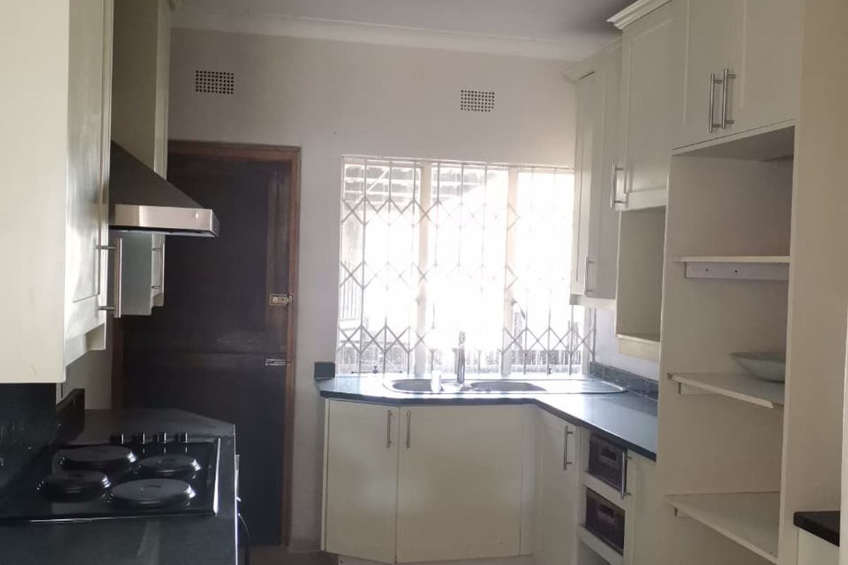 A functional kitchen featuring built-in cabinetry, dark countertops, an electric hob with extractor fan, and tiled flooring, offering a clean canvas for updates.