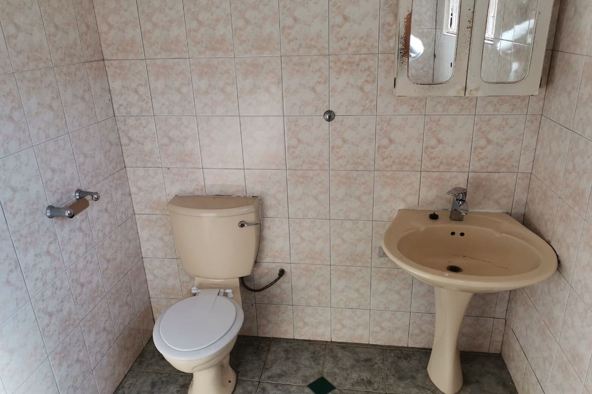 A dated bathroom featuring a pedestal washbasin, toilet, and full-height wall tiling, requiring modernization of fixtures and finishes.