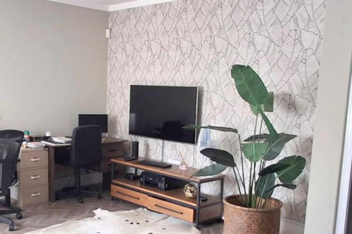 A living room area featuring a decorative patterned feature wall and herringbone flooring, currently utilized as a multi-functional space.
