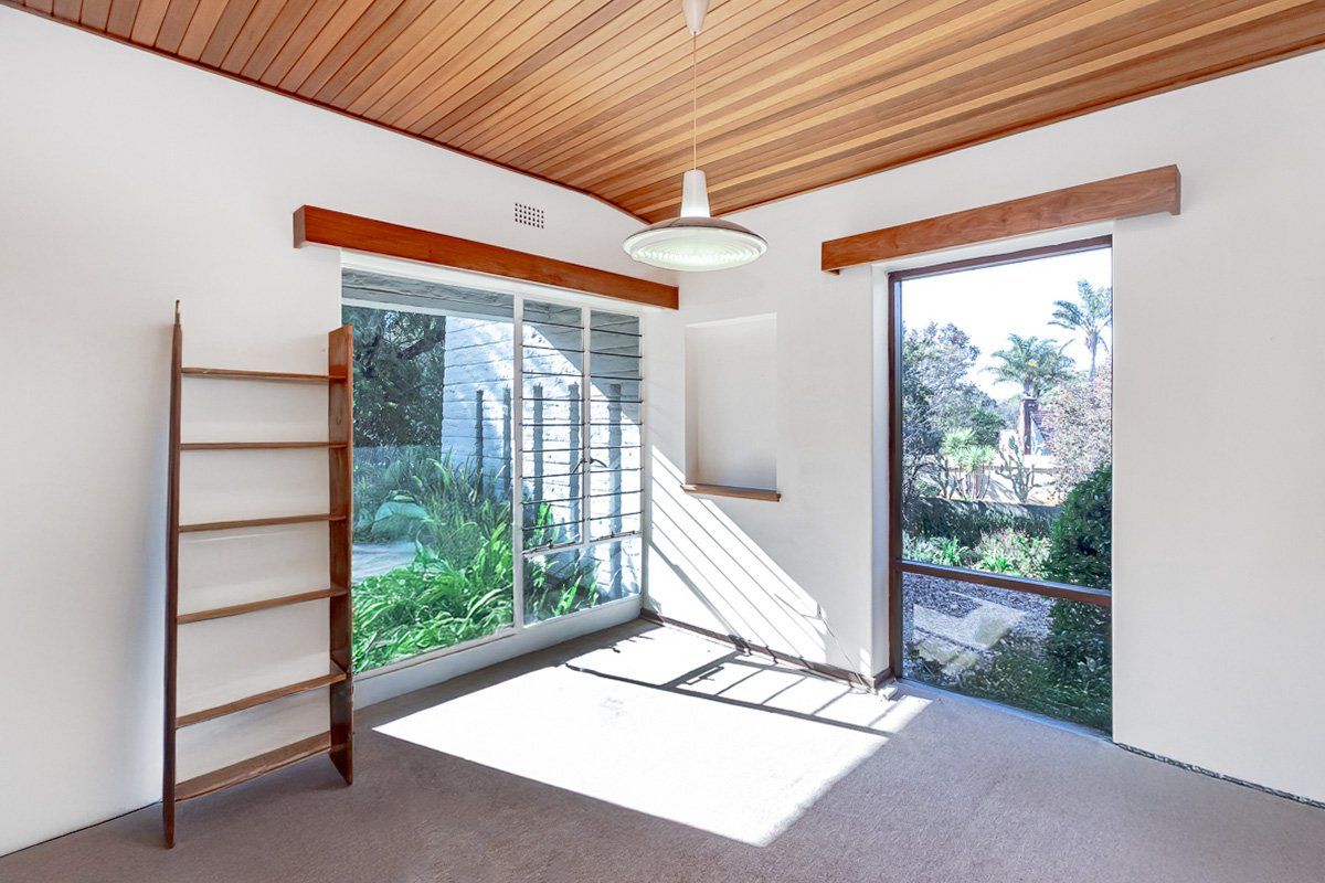 A bright, empty living room featuring a distinctive timber-clad ceiling, large windows with garden views, and neutral wall finishes.