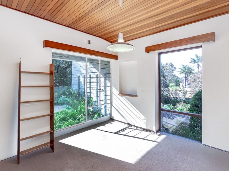 A bright, empty living room featuring a distinctive timber-clad ceiling, large windows with garden views, and neutral wall finishes.
