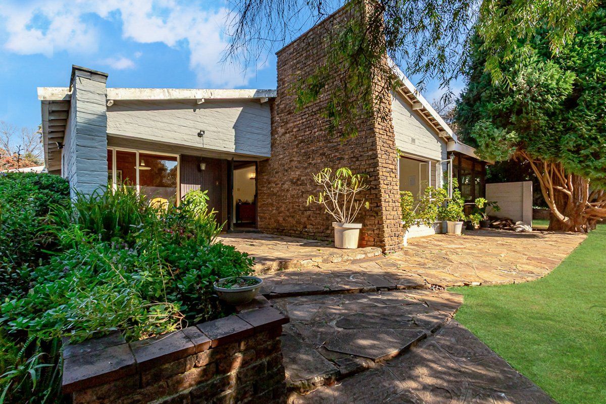 Rear exterior view featuring a stone patio, prominent brick chimney, and established garden area with sliding glass door access to the home.