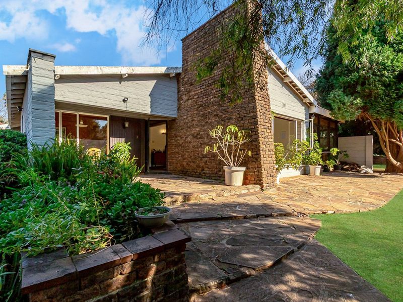 Rear exterior view featuring a stone patio, prominent brick chimney, and established garden area with sliding glass door access to the home.