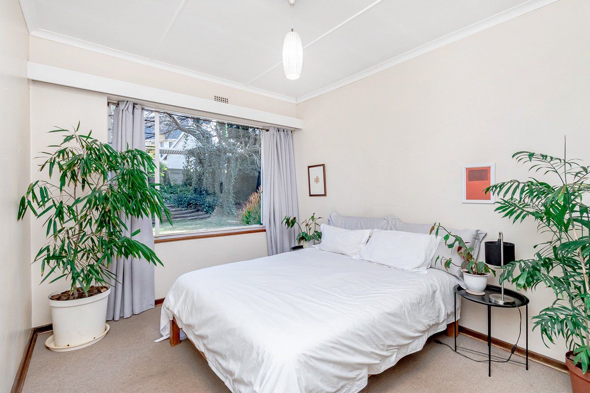 A well-lit bedroom featuring neutral walls, carpeted flooring, and a large window providing natural light and garden views.