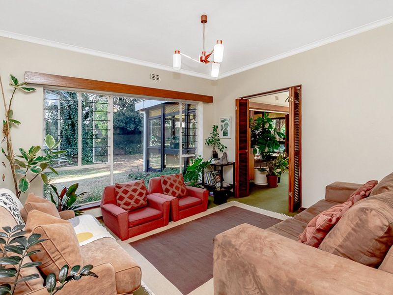 A comfortable living room featuring a large picture window with garden views and timber louvered doors leading to an adjacent space.