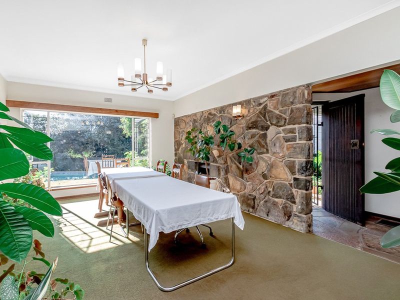 Spacious dining room featuring a prominent stone feature wall, large picture window overlooking the pool area, and classic cove cornicing.