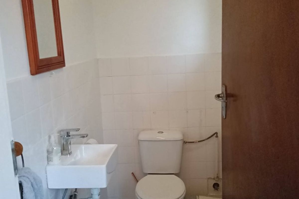 A compact guest bathroom featuring a wall-mounted basin, toilet, and tiled finishes, requiring minor cosmetic updates to conceal exposed plumbing.