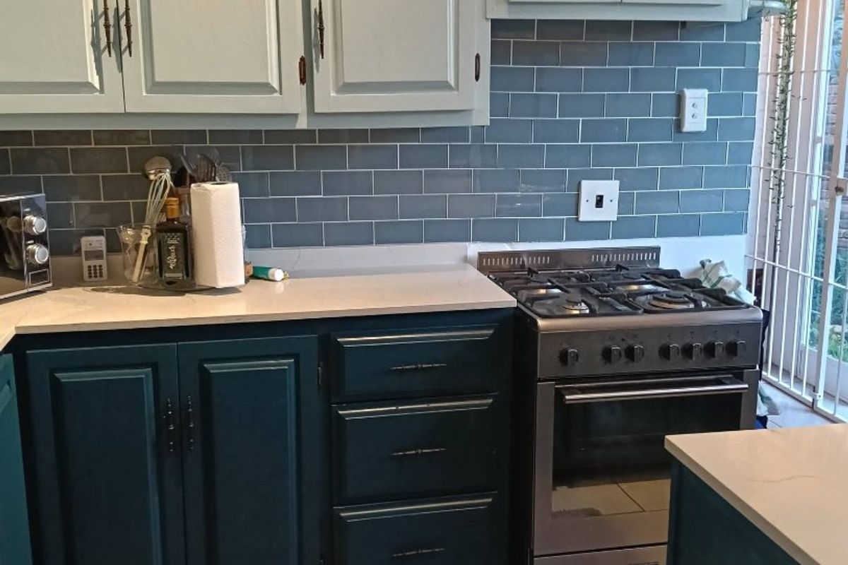 A functional kitchen featuring two-tone cabinetry, a gas stove with oven, subway tile backsplash, and light-colored quartz countertops.