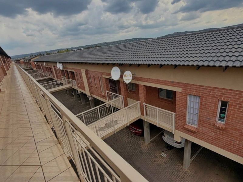 An elevated view of the apartment complex exterior, featuring brick facades, tiled walkways with metal railings, and covered ground-level parking bays.
