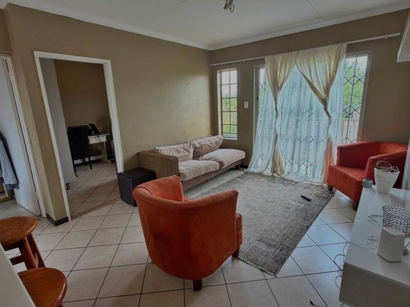 A living room featuring tiled flooring, cove cornicing, and a sliding glass door with a security gate leading to an outdoor area.