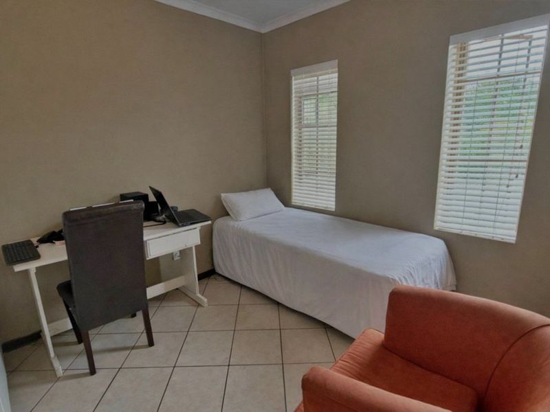 A functional bedroom featuring tiled flooring, neutral wall tones, and dual windows fitted with venetian blinds.