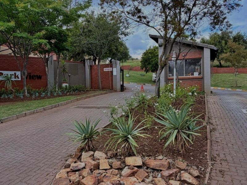 The entrance to Park View complex featuring a secure gatehouse, brick boundary walls, paved driveway, and established landscaped gardens.