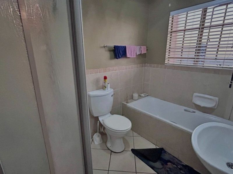 A functional bathroom featuring a bathtub, pedestal basin, and toilet with neutral wall tiles and tiled flooring.