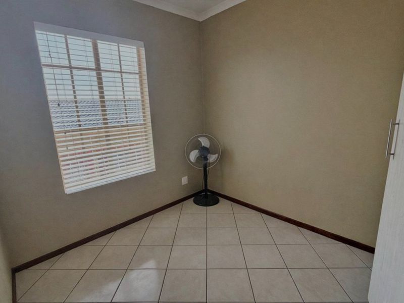 A clean, empty bedroom featuring neutral tiled flooring, a built-in cupboard, and a window fitted with venetian blinds.