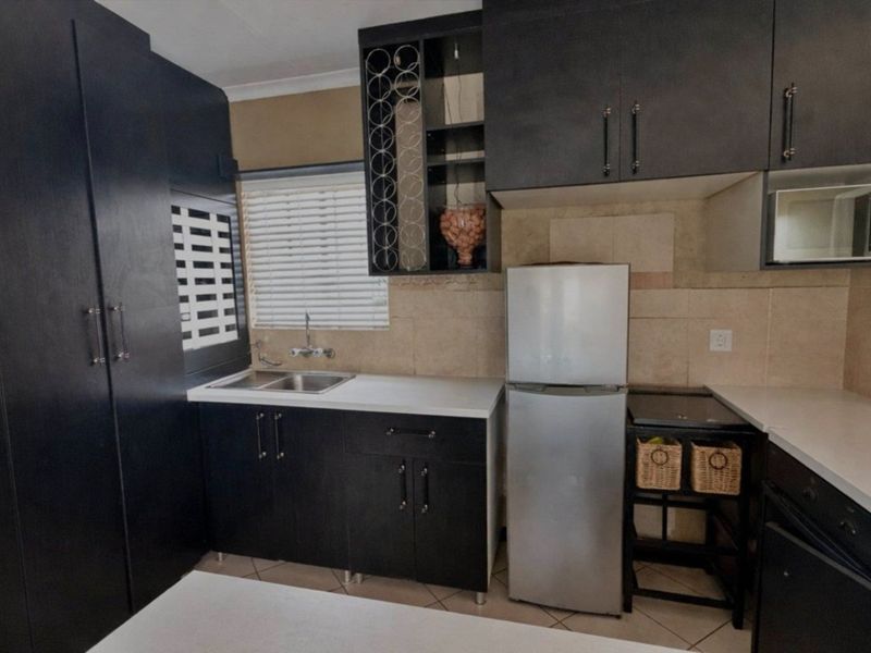Compact kitchen featuring dark cabinetry, tiled backsplash, built-in microwave, and a double sink with a window for natural light.