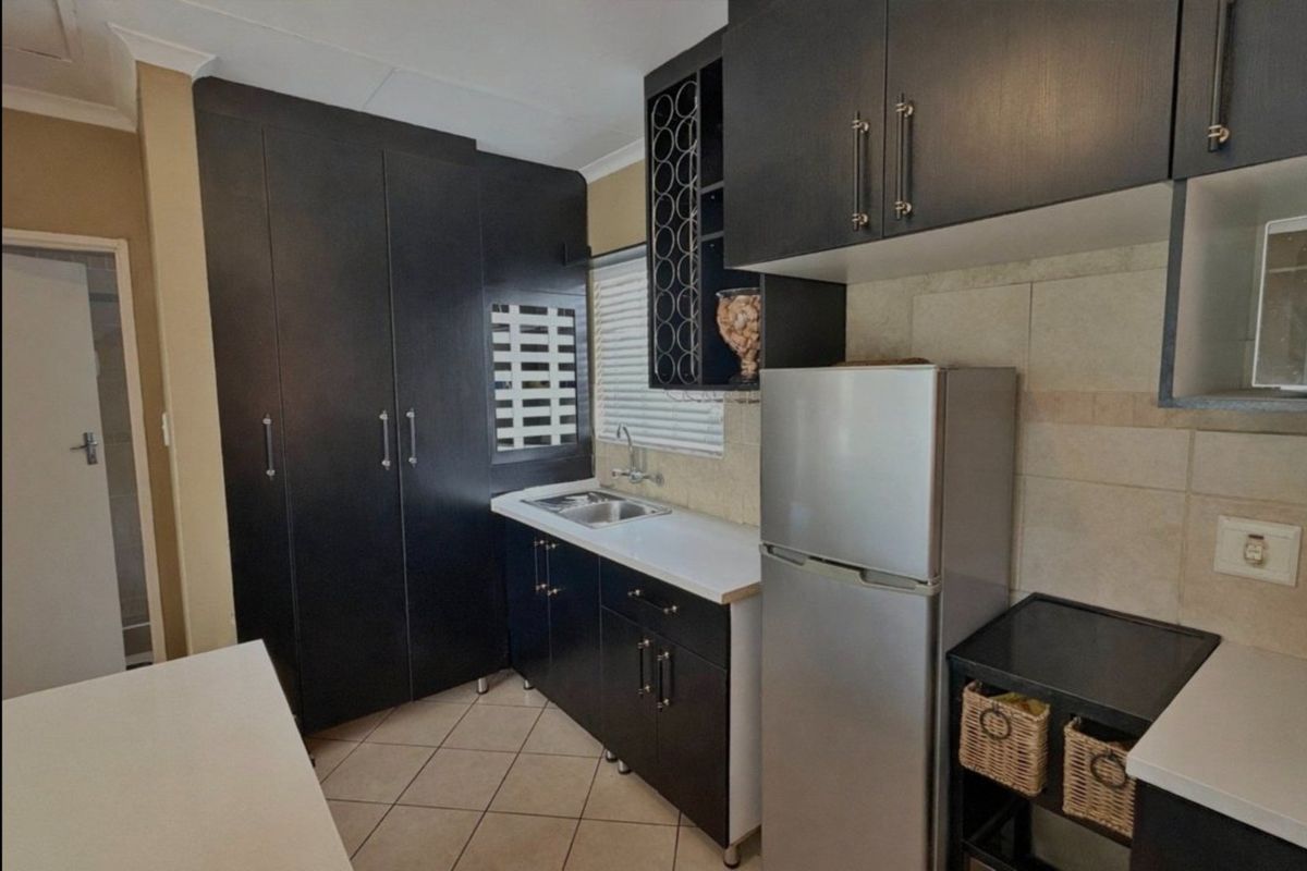A compact kitchen featuring dark cabinetry, tiled backsplash, stainless steel sink, and tiled flooring, offering efficient storage and workspace.