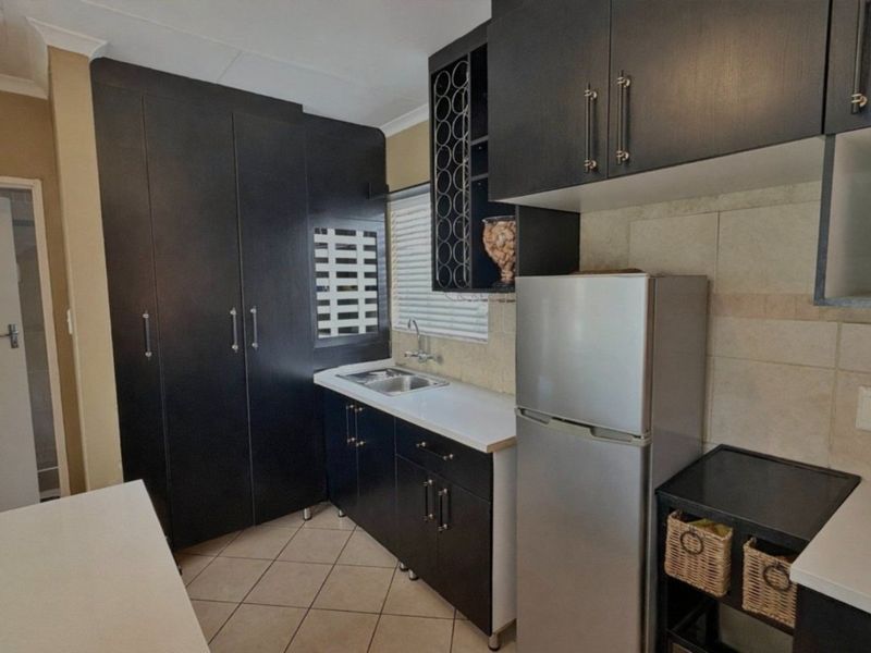 A compact kitchen featuring dark cabinetry, tiled backsplash, stainless steel sink, and tiled flooring, offering efficient storage and workspace.
