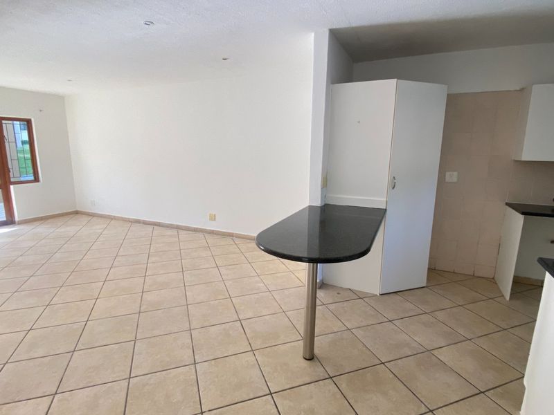 An open-plan living and kitchen area featuring tiled flooring, a granite breakfast bar, and direct access to an outdoor patio through a sliding door.