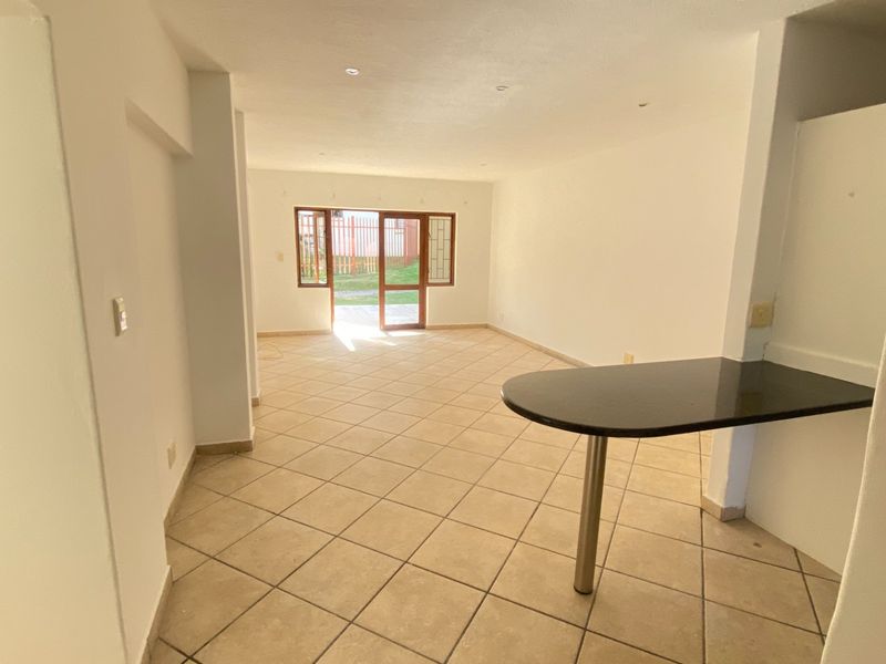 Spacious open-plan living area featuring tiled flooring, a built-in breakfast bar, and direct access to the outdoor space through a sliding glass door.