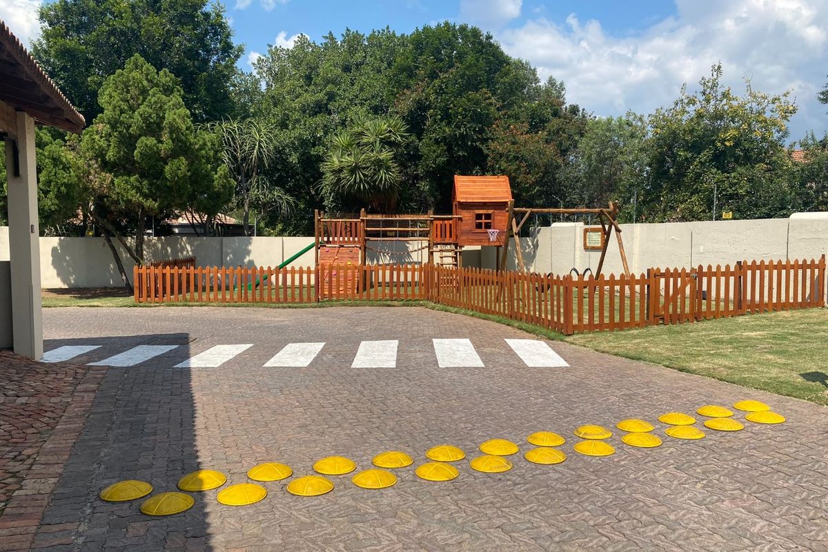 A well-maintained outdoor area featuring a paved driveway, perimeter wall, and a fenced-in playground section with wooden play equipment.