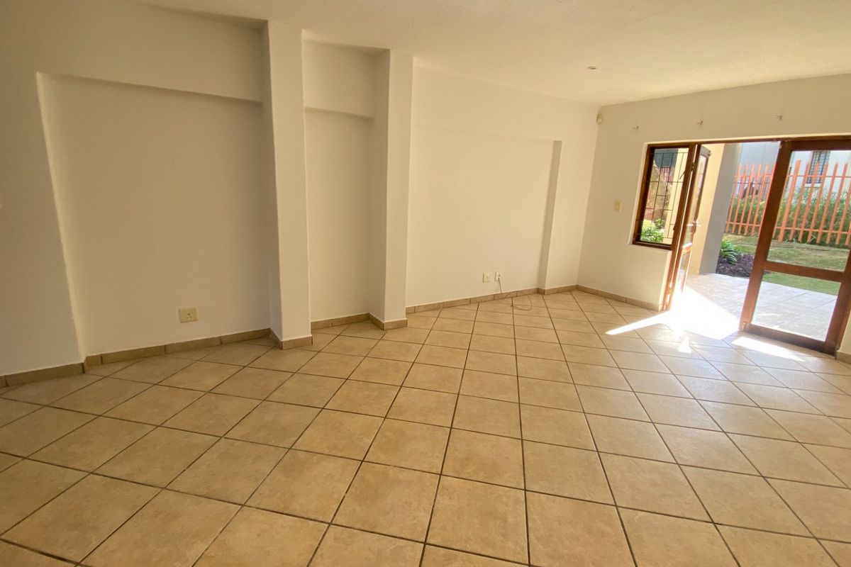 An empty, open-plan living area featuring neutral ceramic floor tiles and direct access to an outdoor patio through a wooden door frame.