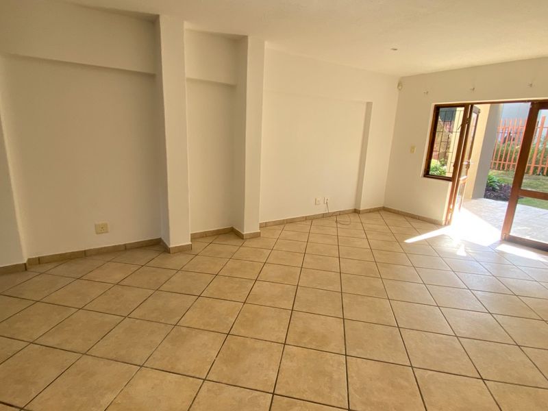 An empty, open-plan living area featuring neutral ceramic floor tiles and direct access to an outdoor patio through a wooden door frame.