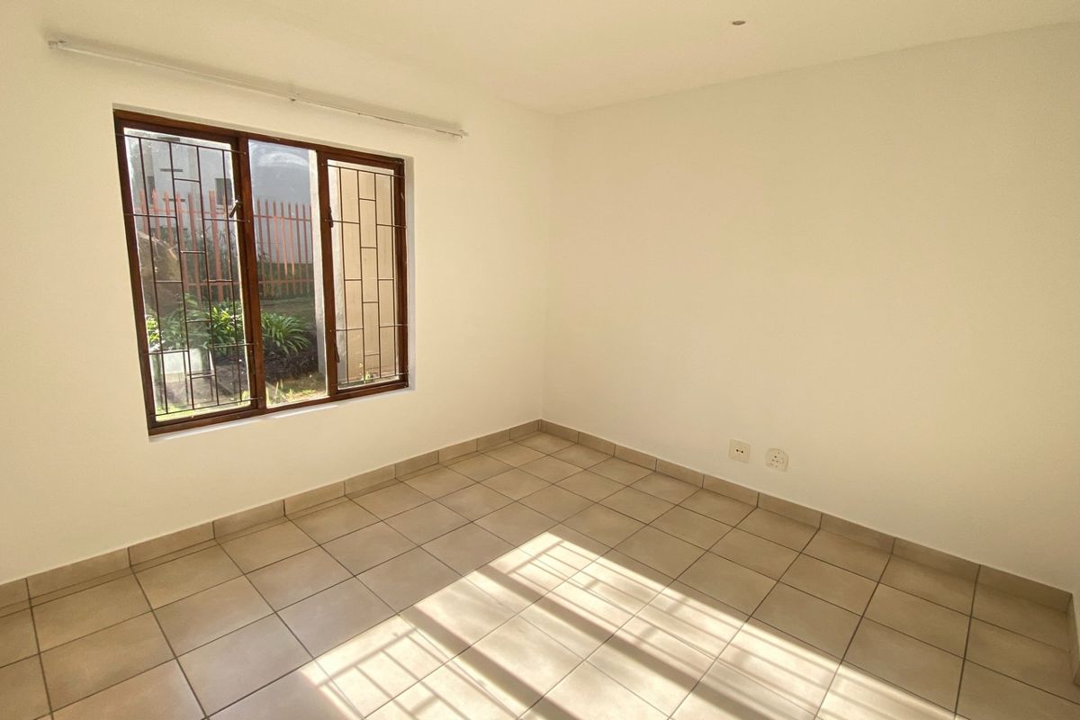 A bright, empty bedroom featuring neutral tiled flooring and a window fitted with security bars, offering a clean canvas for personalization.