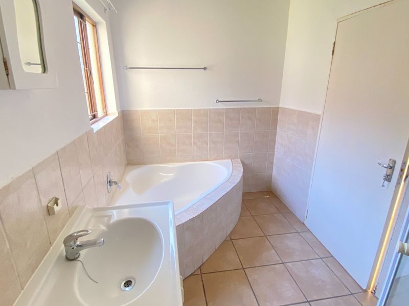 A clean, functional bathroom featuring a corner bathtub, pedestal basin, and neutral wall and floor tiling.