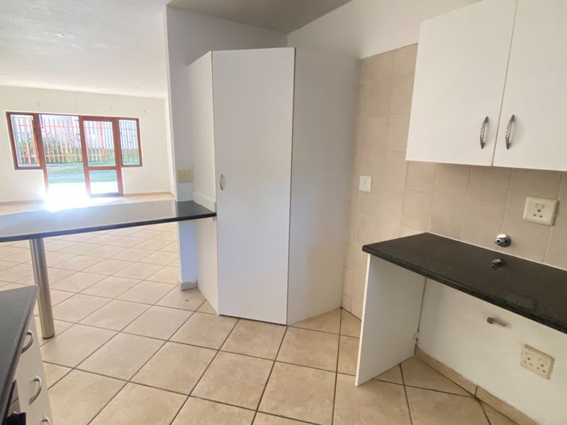 Open plan kitchen and living area featuring tiled flooring, built-in cabinetry, and dark laminate countertops in a neutral, vacant space.