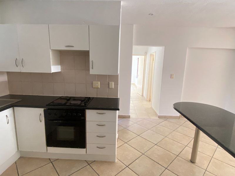A functional kitchen featuring white cabinetry, dark countertops, a built-in oven and hob, and an attached breakfast bar, leading into a tiled hallway.