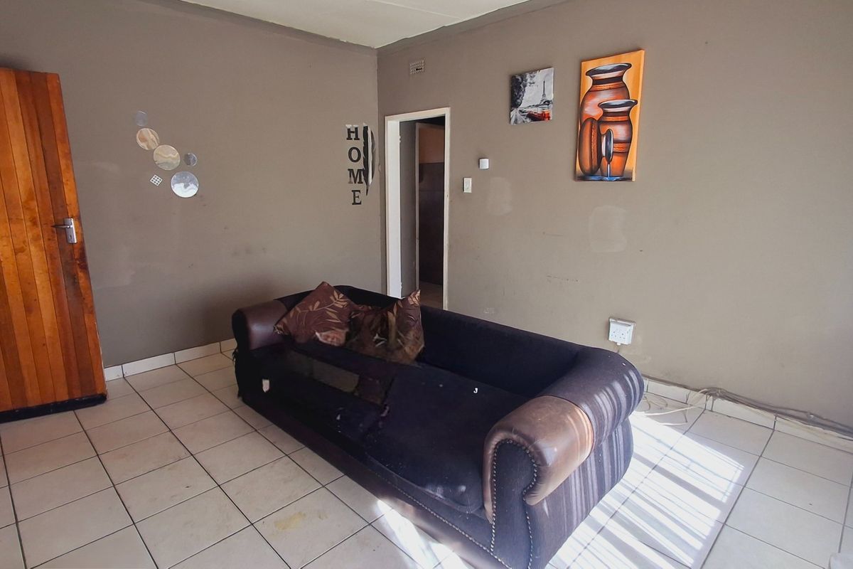 A living room area featuring tiled flooring and a wooden door, requiring cosmetic updates to the wall finishes and flooring.