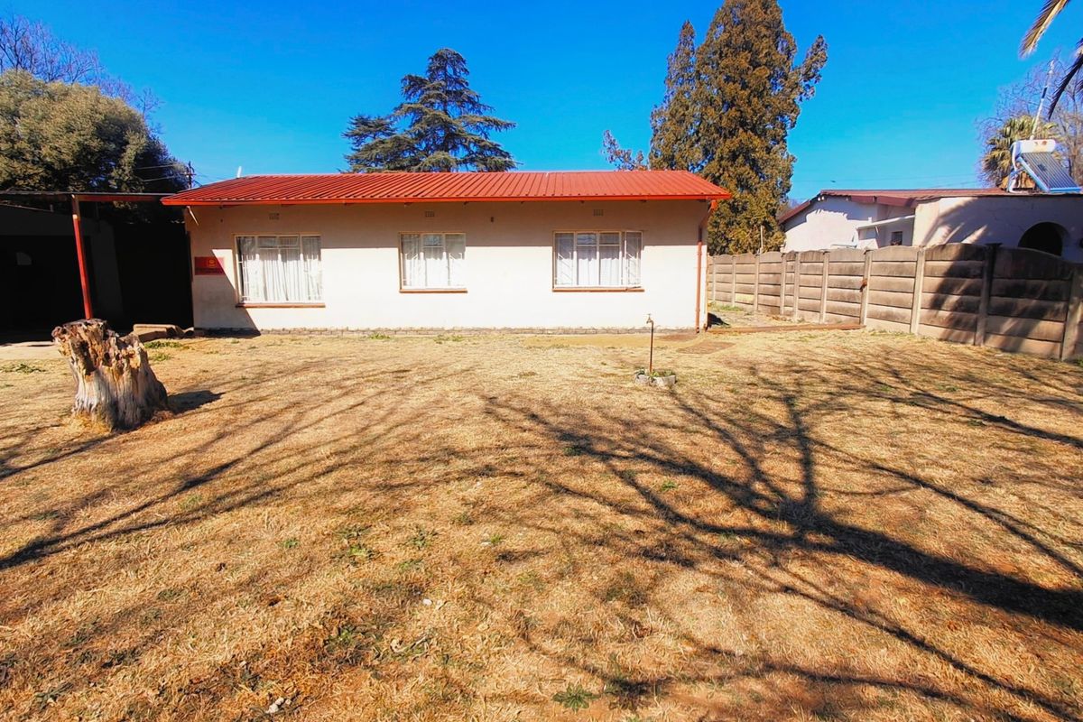 Rear view of the property featuring a corrugated metal roof, precast concrete boundary wall, and a spacious backyard area.