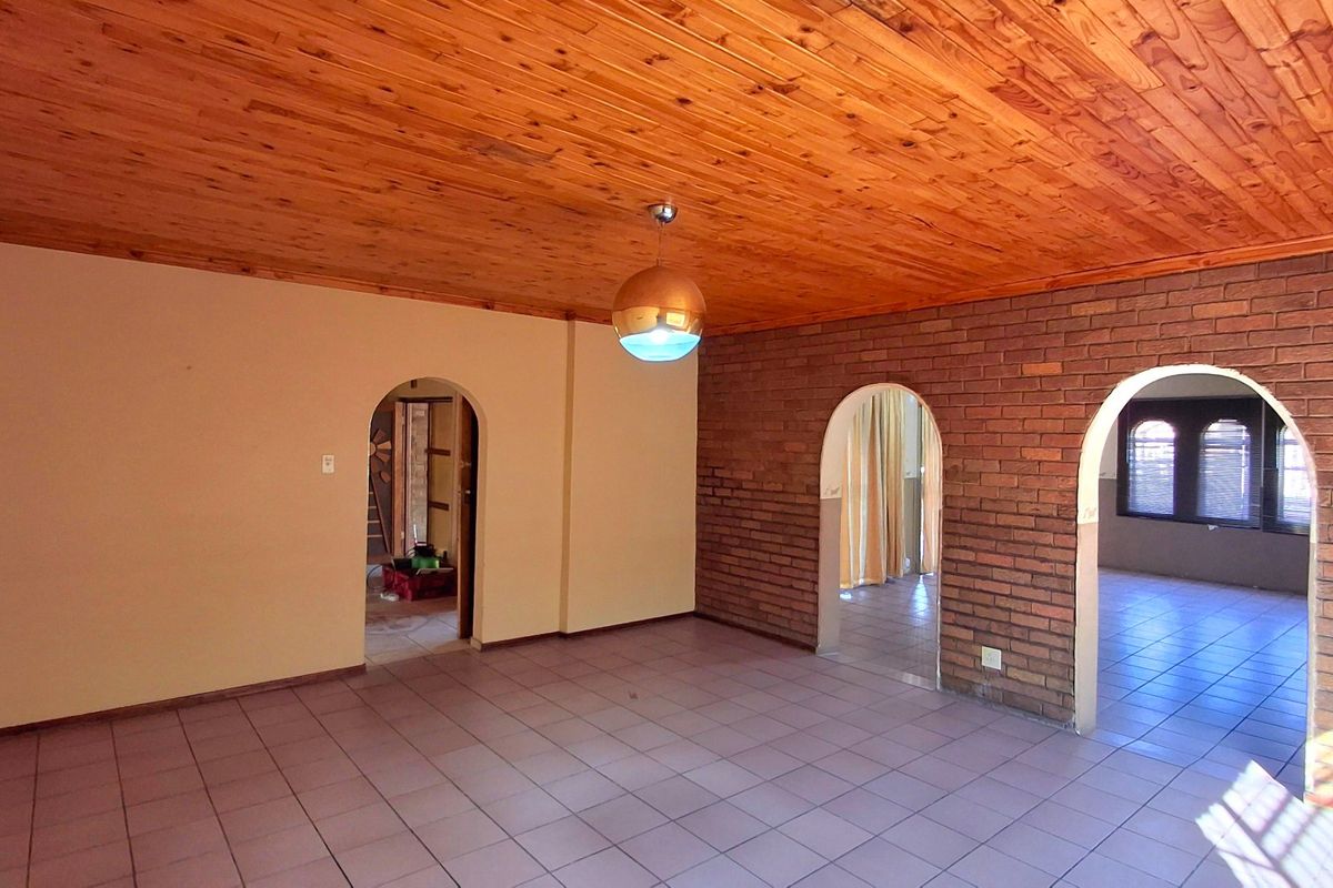 Spacious living area featuring an exposed timber ceiling, brick feature wall, and arched doorways leading to adjacent rooms with tiled flooring throughout.