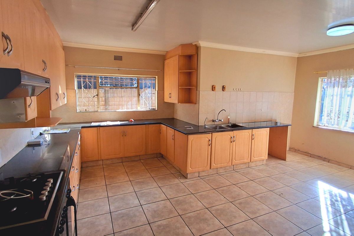 Spacious kitchen featuring extensive wooden cabinetry, dark granite countertops, double sink, and tiled flooring, offering a functional layout ready for modernization.
