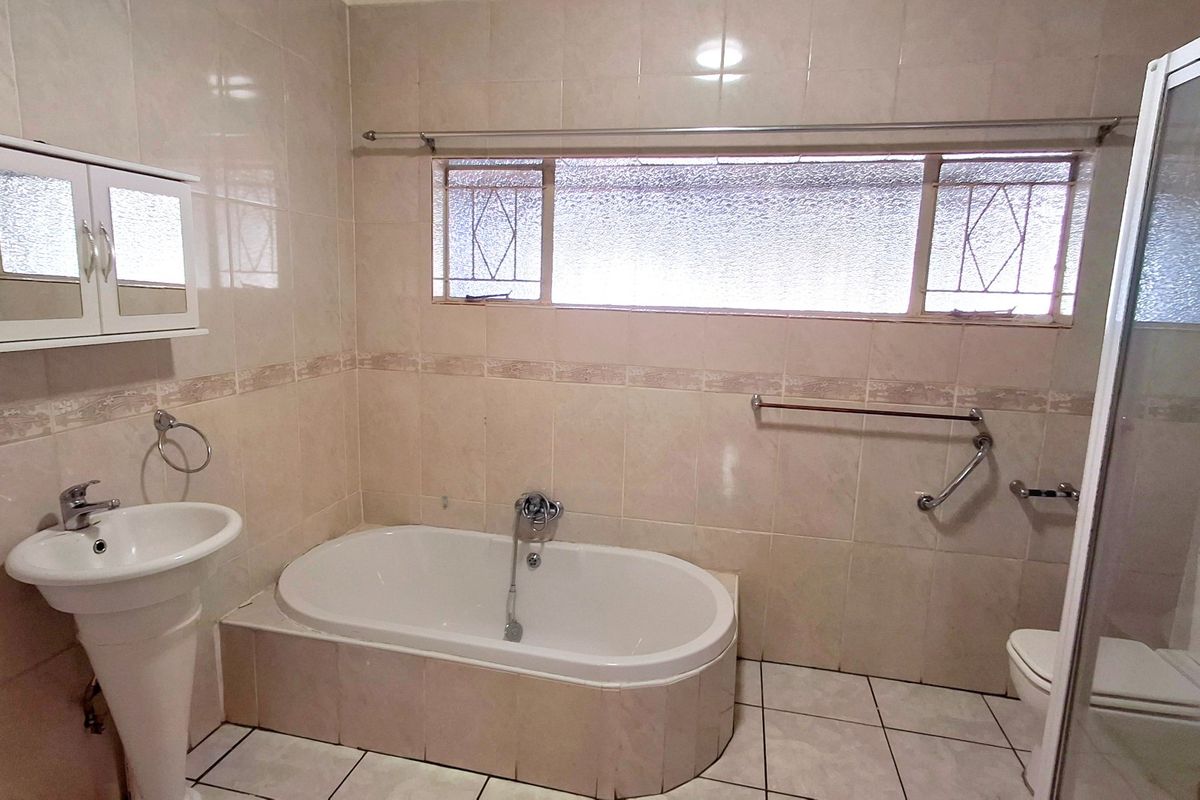 A functional bathroom featuring a built-in bathtub, pedestal basin, separate shower enclosure, and tiled finishes throughout.