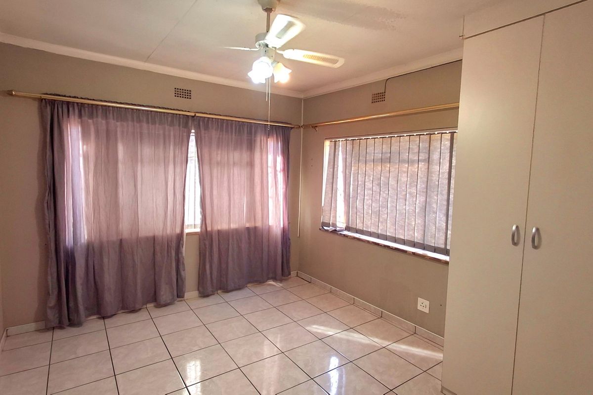 A spacious, empty bedroom featuring neutral tiled flooring, a ceiling fan, and a built-in wardrobe, offering a clean canvas for personalization.