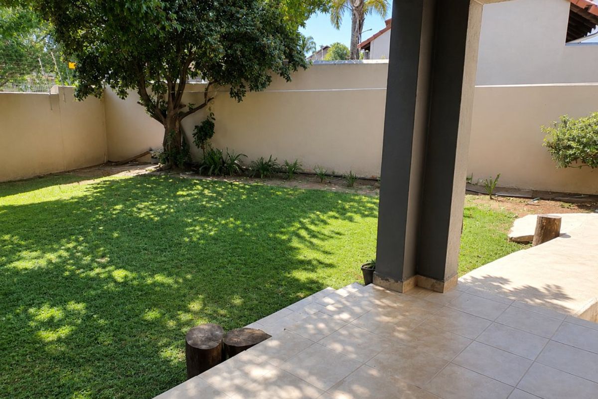 A covered tiled patio overlooking a private garden with a lawn and perimeter wall, providing a pleasant outdoor living space.