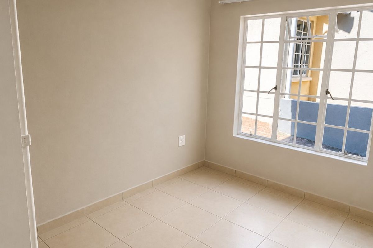 A clean, empty bedroom featuring neutral tiled flooring, a window with security bars, and a curtain rail, ready for personalization.